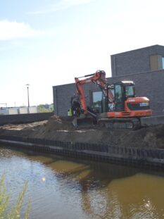Mobiele kraan in een tuin bezig met grondwerk ter voorbereiding op tuinaanleg.