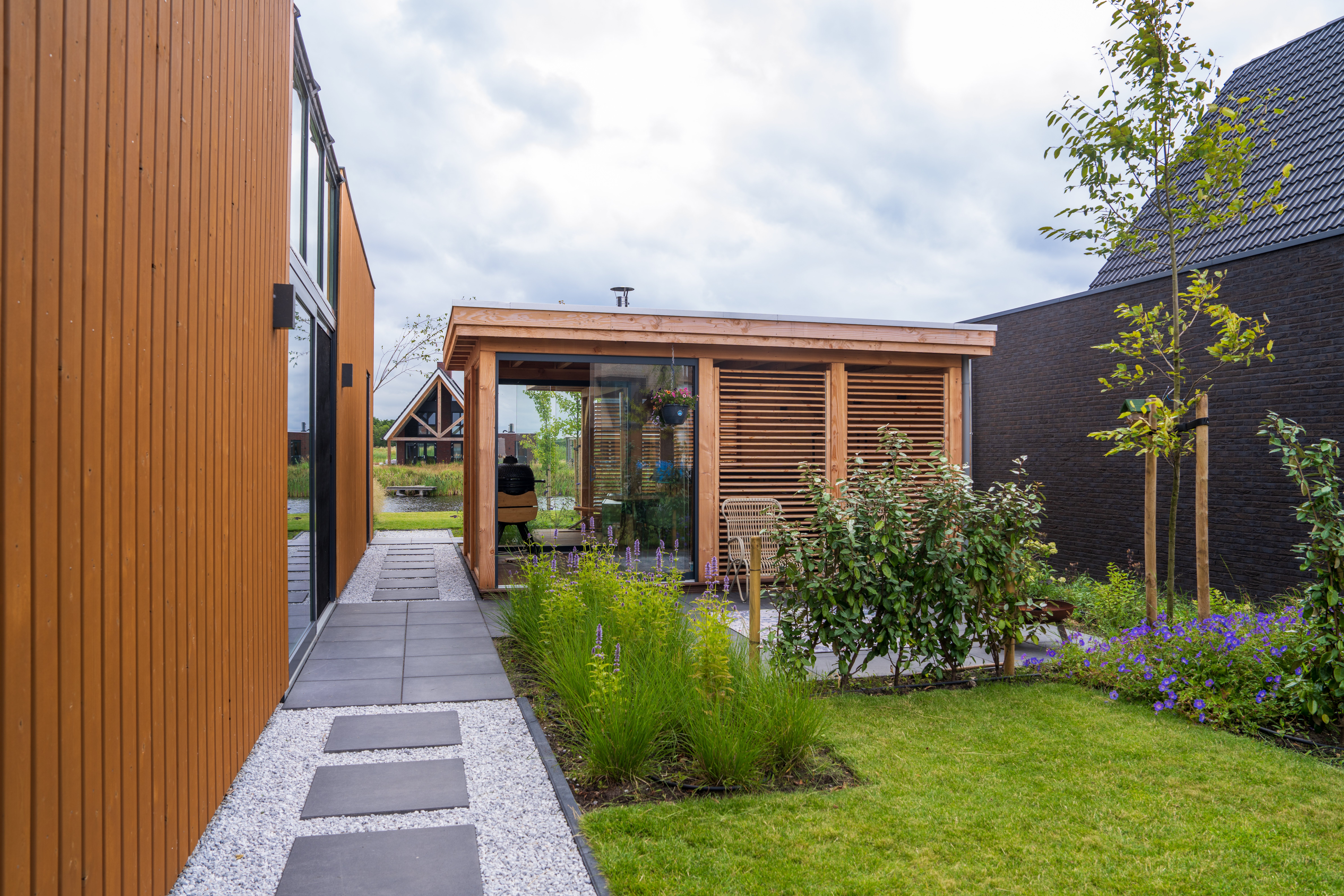 Tuinpad richting het water met overkapping van glas en shutters in een moderne tuin